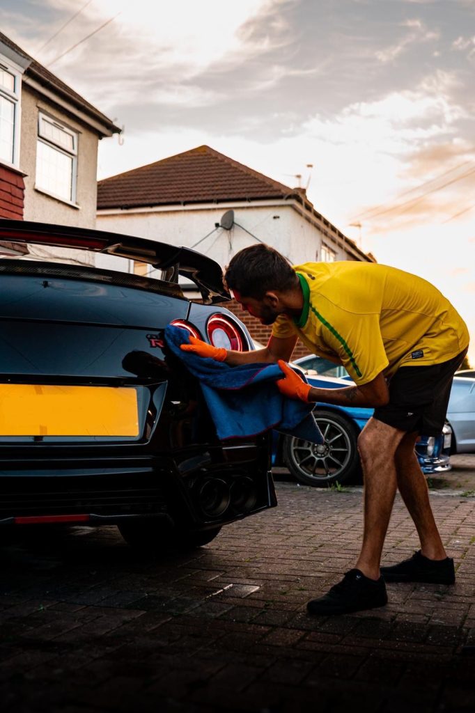 Cris drying the rear of a black Nissan GT-R with a microfibre towel in evening light