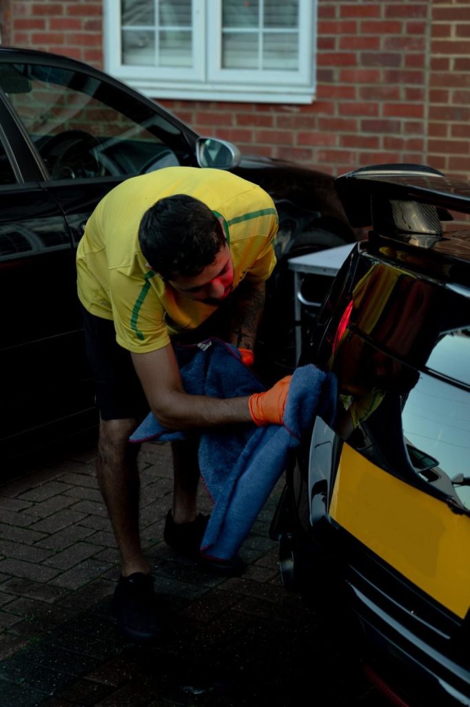 Cris drying the rear quarter panel of a black car with a plush microfibre towel
