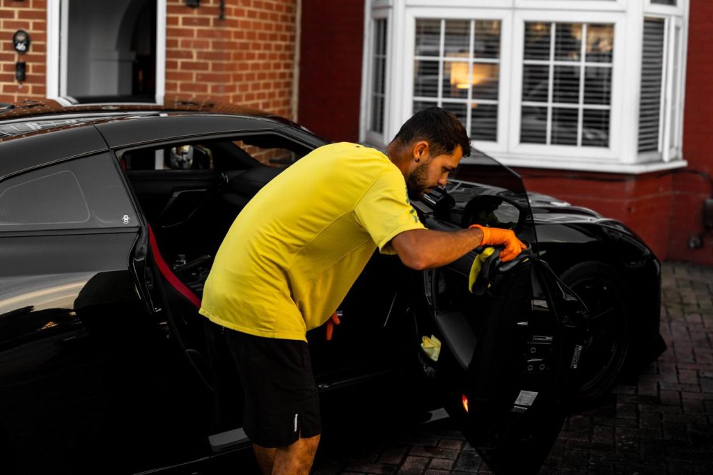 Cris wiping down the door shut of a black sports car with a microfibre cloth