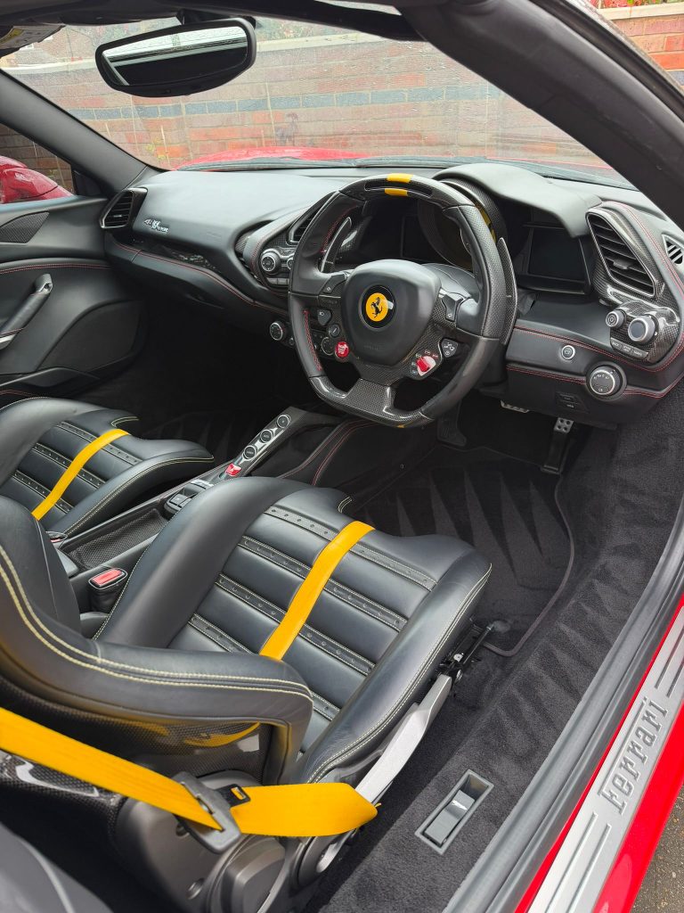 Ferrari 488 cabin with carbon fibre steering wheel and yellow seat belts after an interior detail