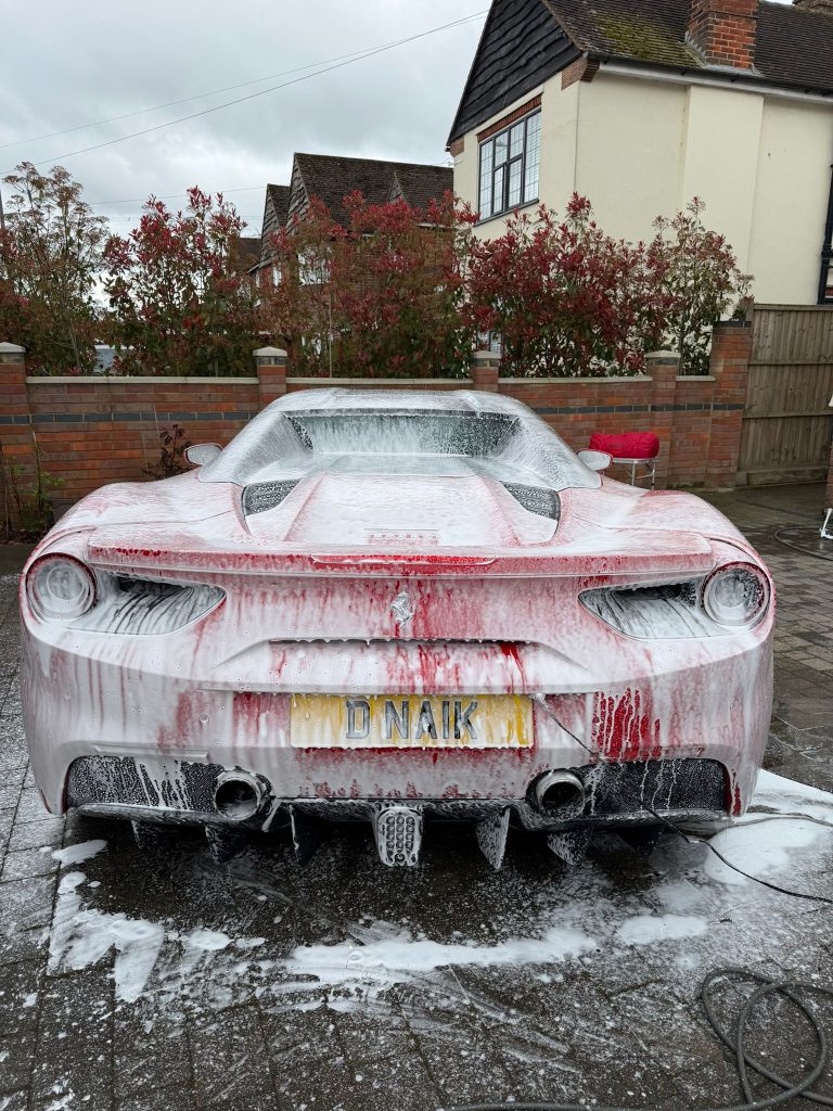 Red Ferrari 488 Spider covered in white snow foam during the pre-wash stage
