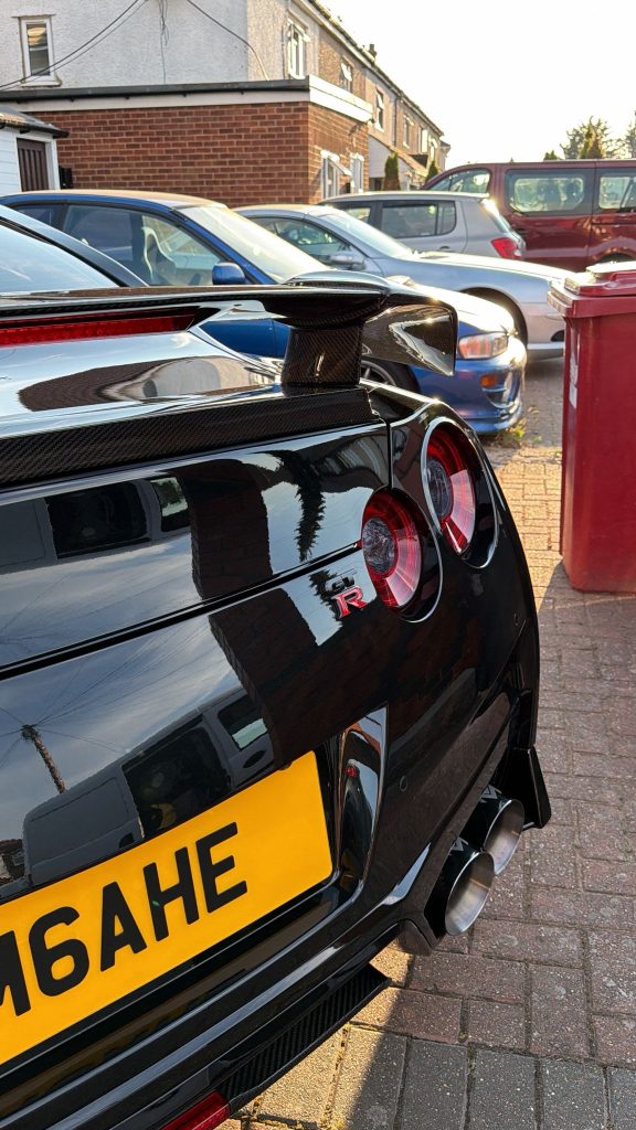 Close-up of a gloss black Nissan GT-R's carbon rear wing and tail lights after polishing