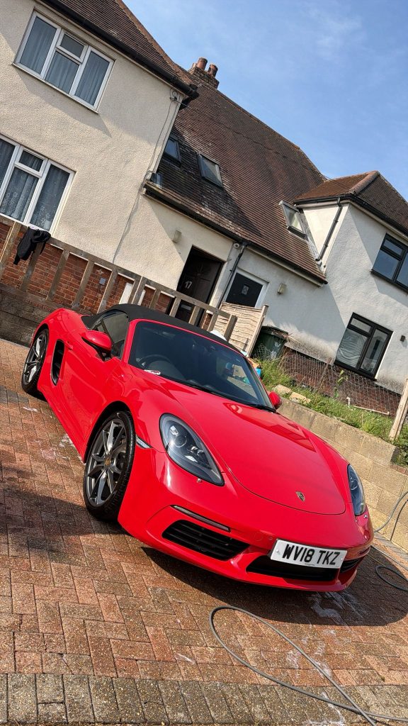 Guards red Porsche 718 Boxster being washed on a block-paved driveway