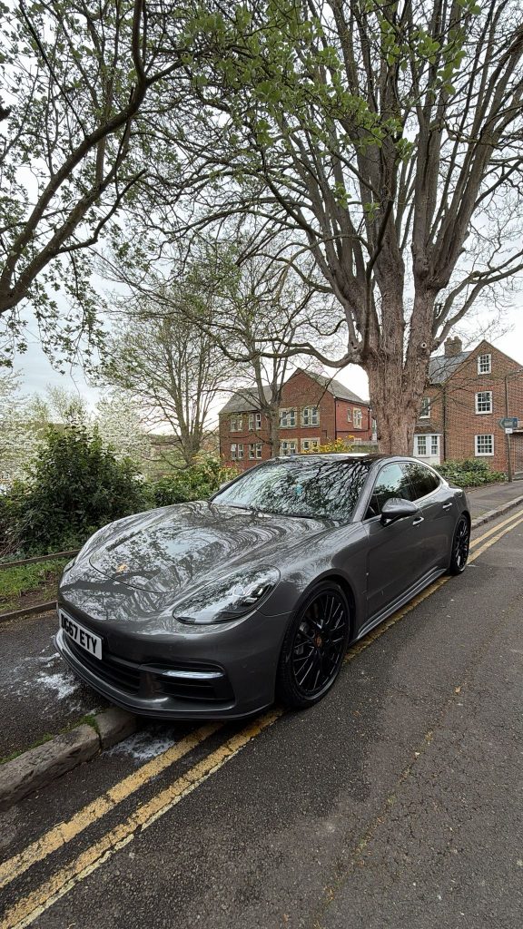 Grey Porsche Panamera parked kerbside, the paintwork mirroring the trees overhead after a detail