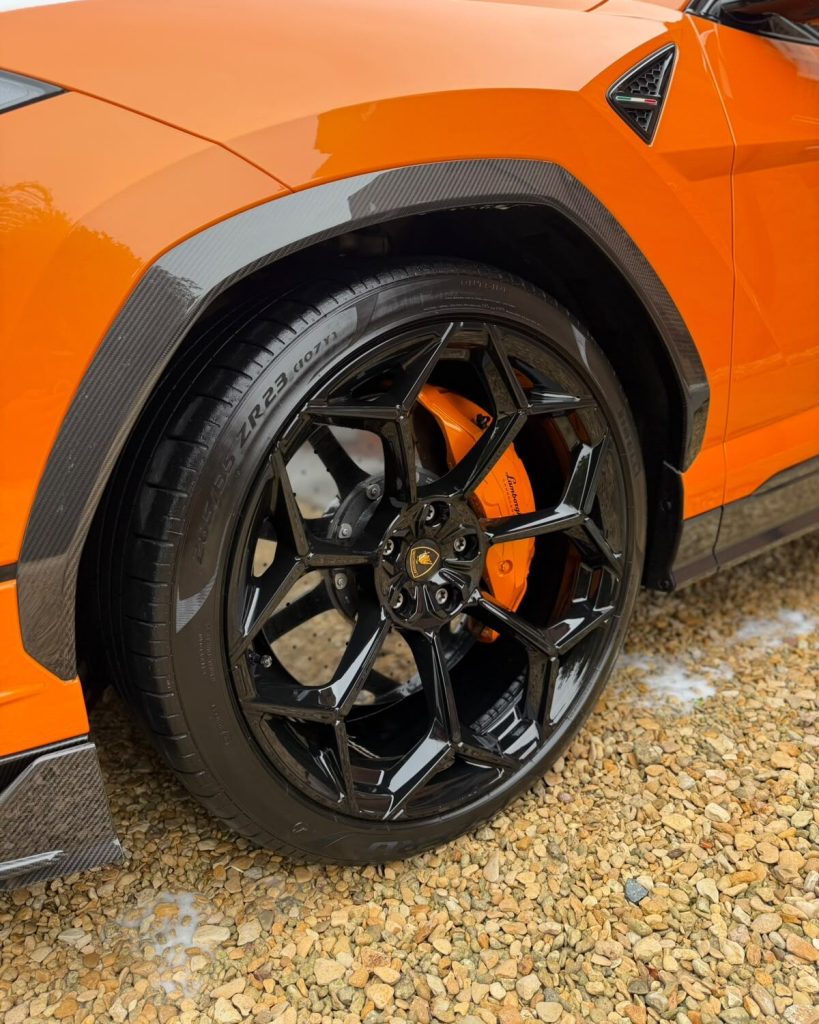 Close-up of a gloss black Lamborghini Urus wheel and orange brake caliper, tyre dressed